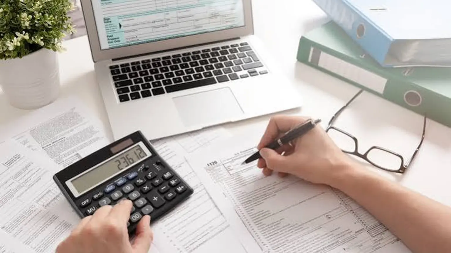 Calculator, tax forms, and a laptop used for accounting work